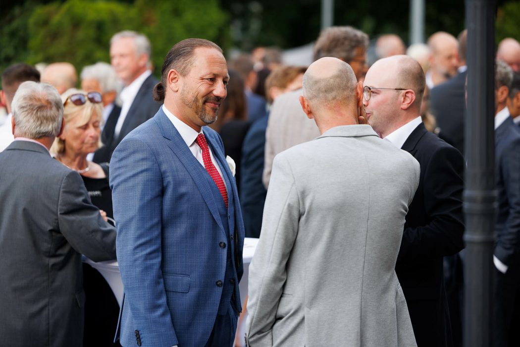 Mehrere Menschen unterhalten sich bei einer Veranstaltung im Freien. Ein Mann im blauen Anzug lächelt und führt ein Gespräch.